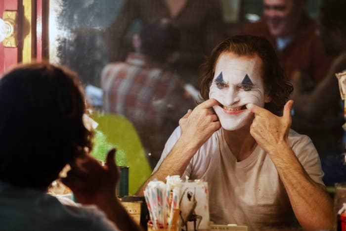 Phoenix as the Joker pulling his face into a smile with clown makeup