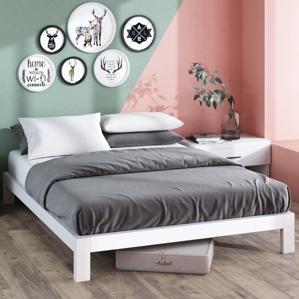 the white bed frame with a mattress and gray bedding on it and circle art decor on the wall above it