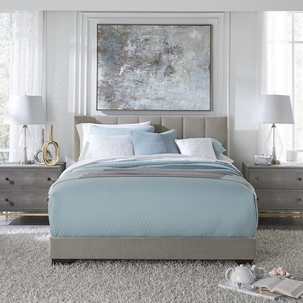 the gray bed frame with blue bedding and two nightstands on the sides of the bed and two lamps on each of the nbightstands