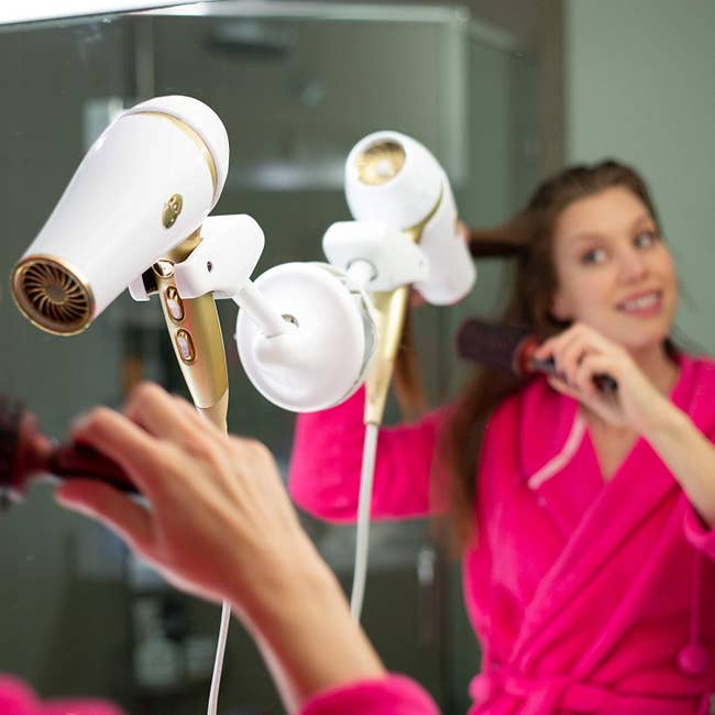 Model brushing their hair with the hair dryer on the holder against the mirror