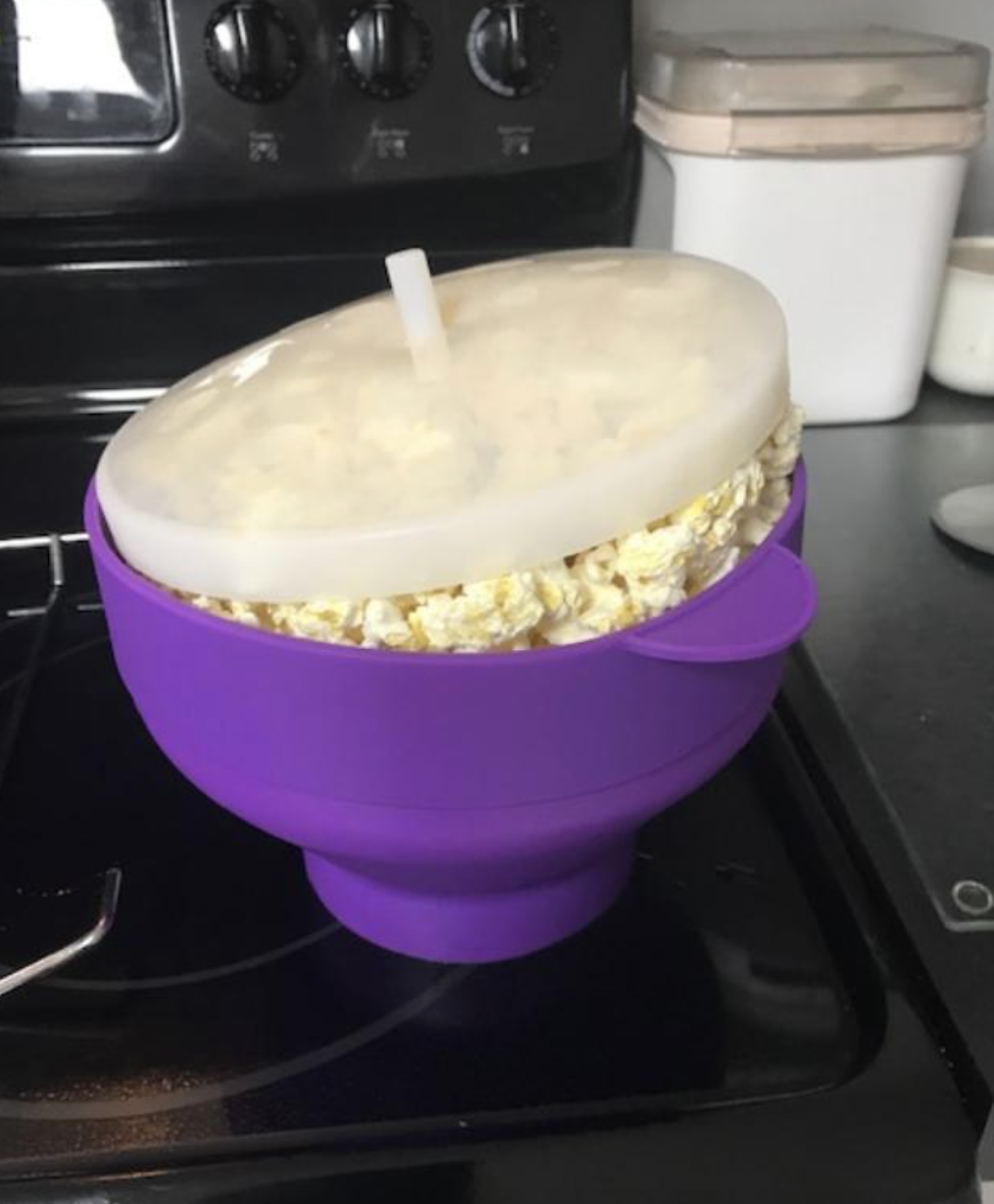 A purple bowl with popped corn inside of it and a clear lid on top