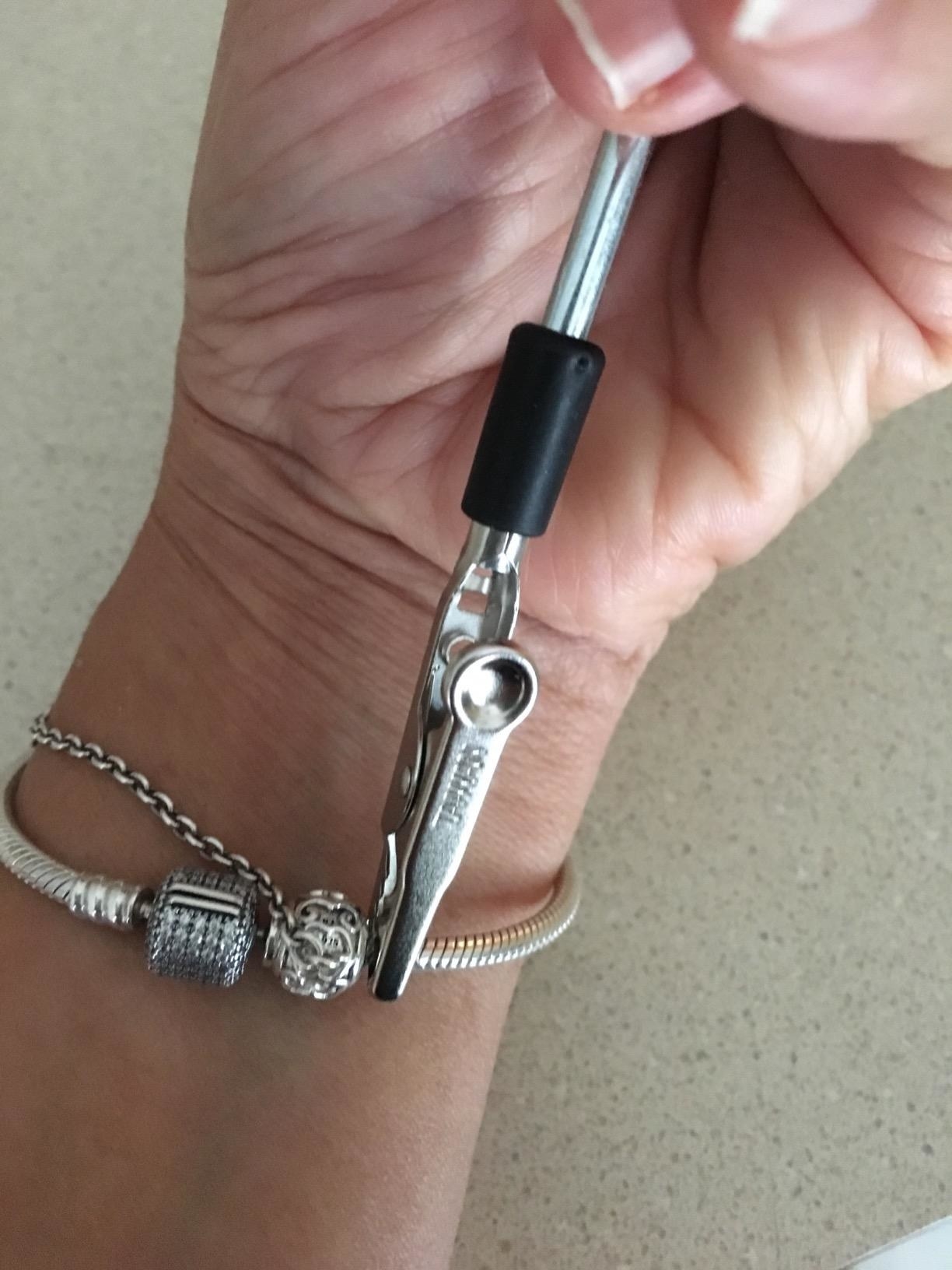 a reviewer uses bracelet tool to loop together silver charm bracelet on wrist