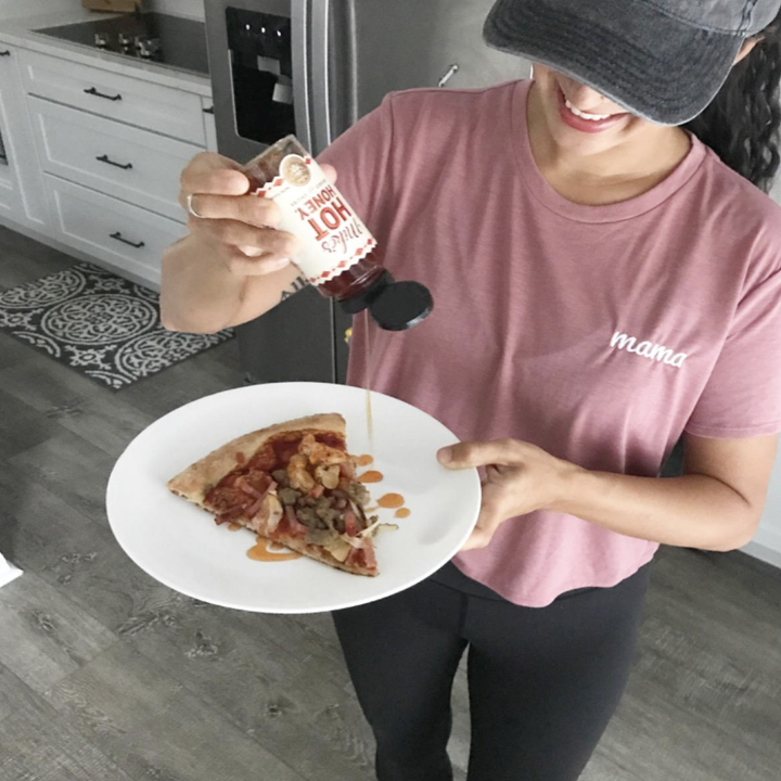 A reviewer drizzling hot honey on pizza