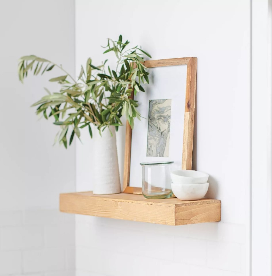 Wooden floating shelf with white vase and plant on it, picture frame, white bowls