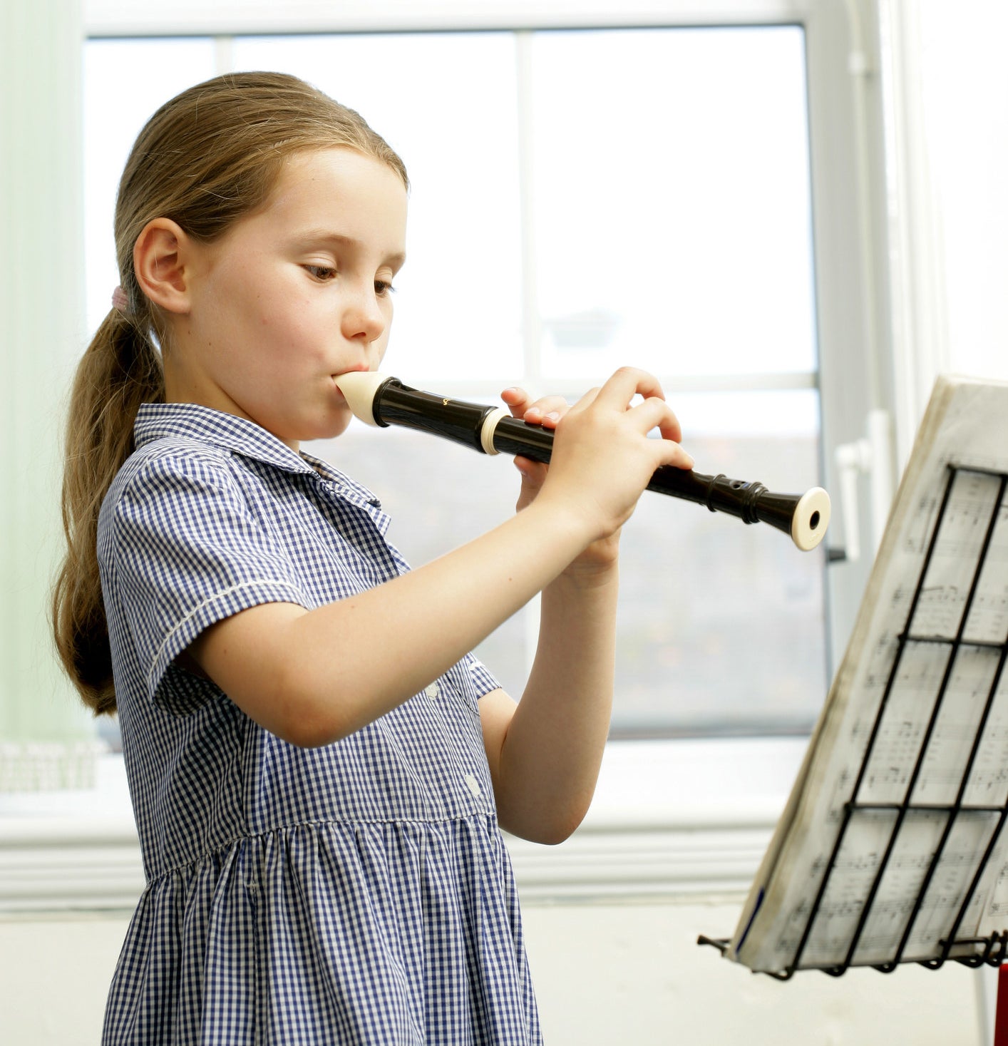 A young girl playing the recorder while looking at sheet music