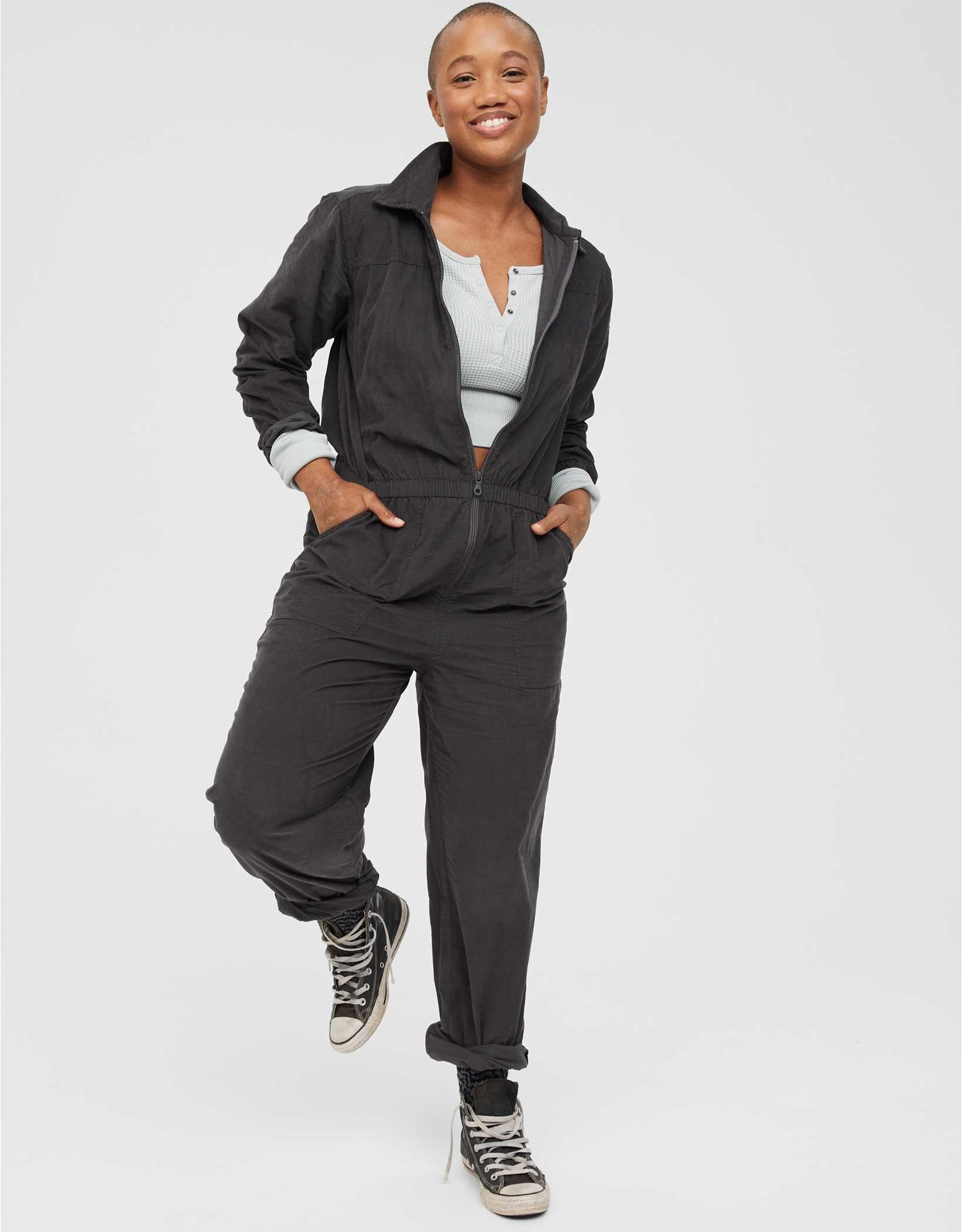 model wearing the jumpsuit in black with black converse and gray long sleeve top underneath