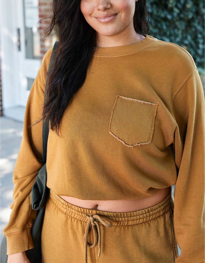 model wearing the sweatshirt in brown with a pocket on the left side and matching sweats carrying a black bag