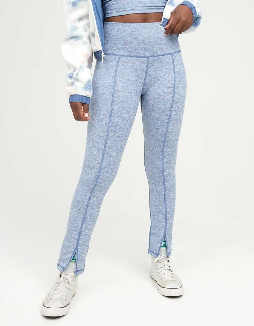 model wearing the leggings in blue with small slits at the ankle over white converse with a matching top and a zip up with white and blue patterning