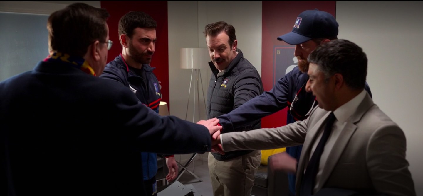 Ted, Leslie, and the other coaches with their hands together in &quot;Ted Lasso.&quot;