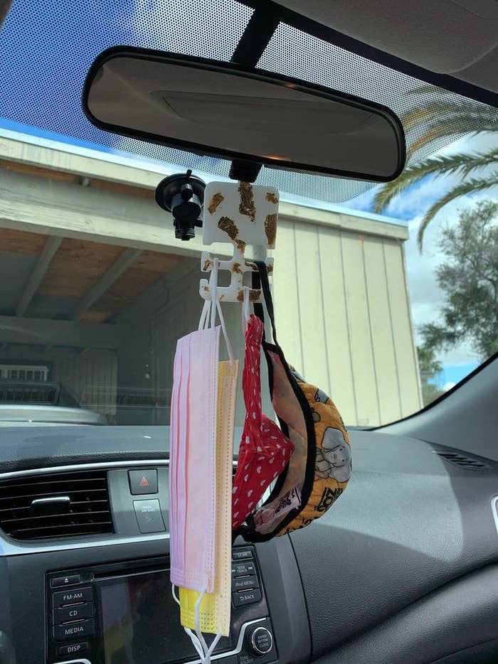 gold and white resin face mask holder with face masks on car mirror