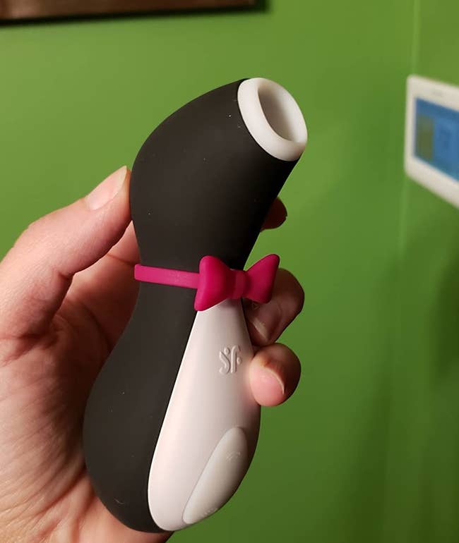 Reviewer holding black and white penguin-shaped suction vibrator