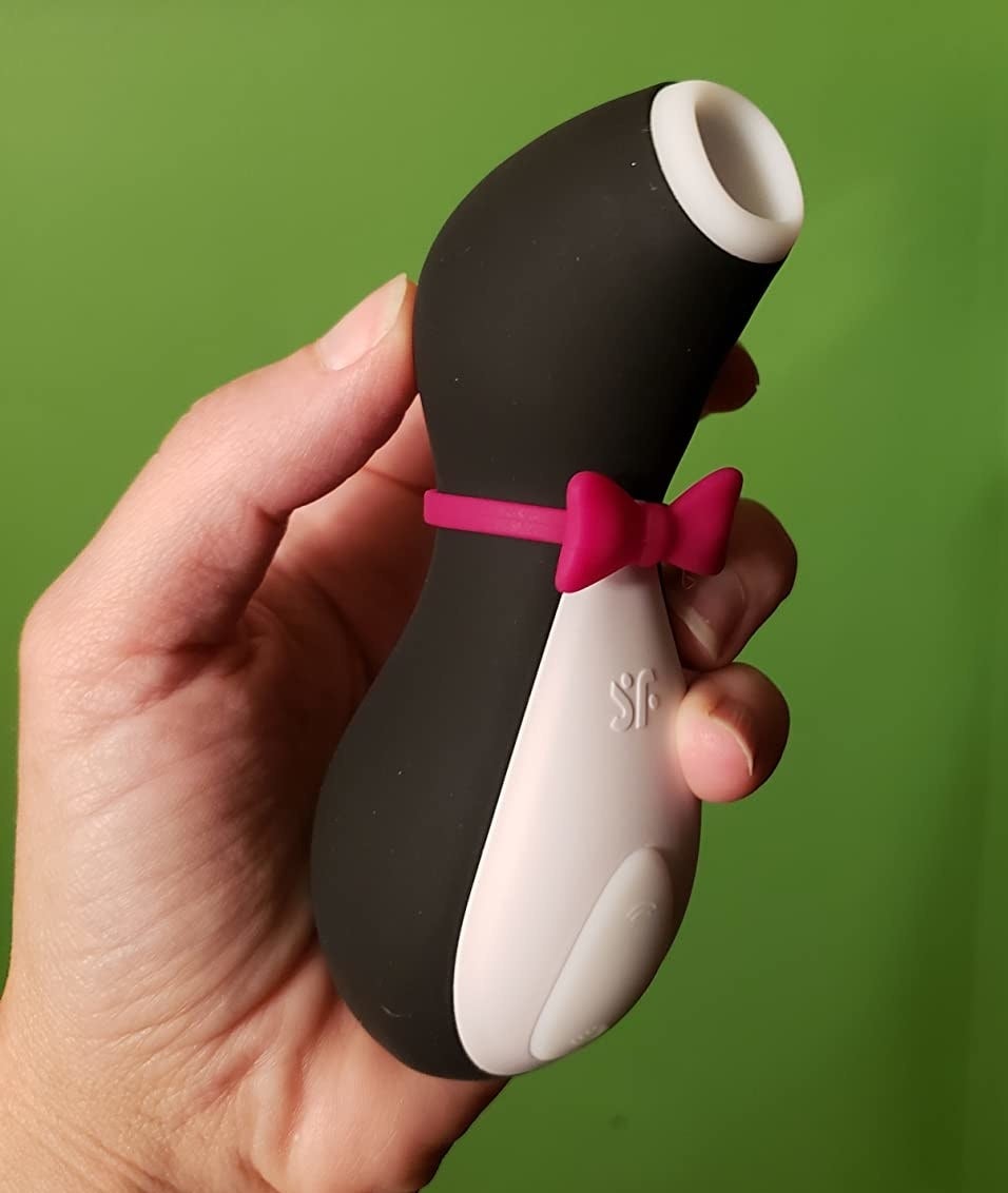 Reviewer holding black and white penguin-shaped suction vibrator