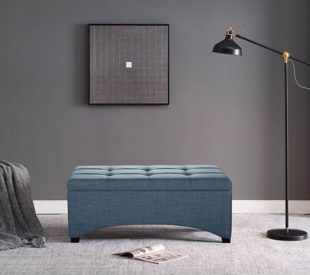 the blue bench with an open magazine in front of it, a framed piece of art hanging above it, and a black standing lamp next to it