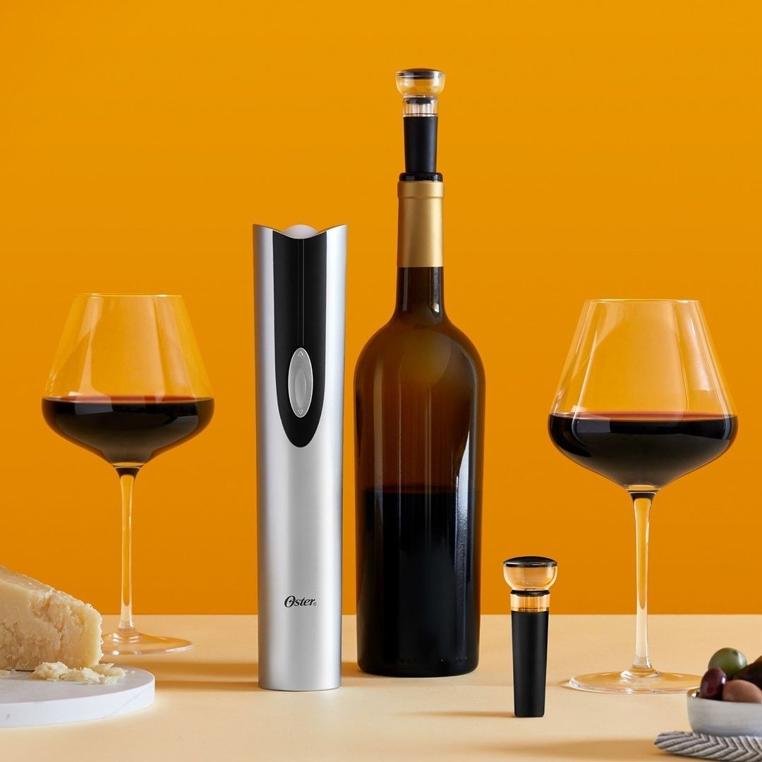 an electric wine opener next to a corked bottle and two full glasses