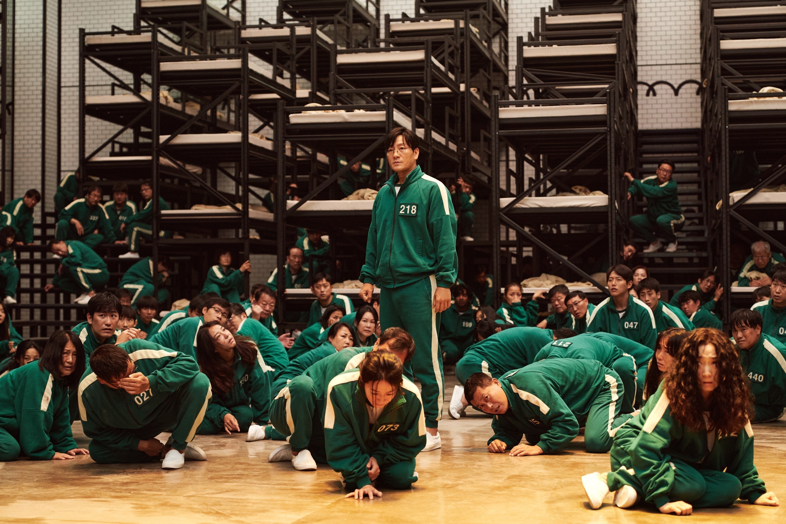 Park Hae-soo stands up in a room full of crouching people wearing tracksuits