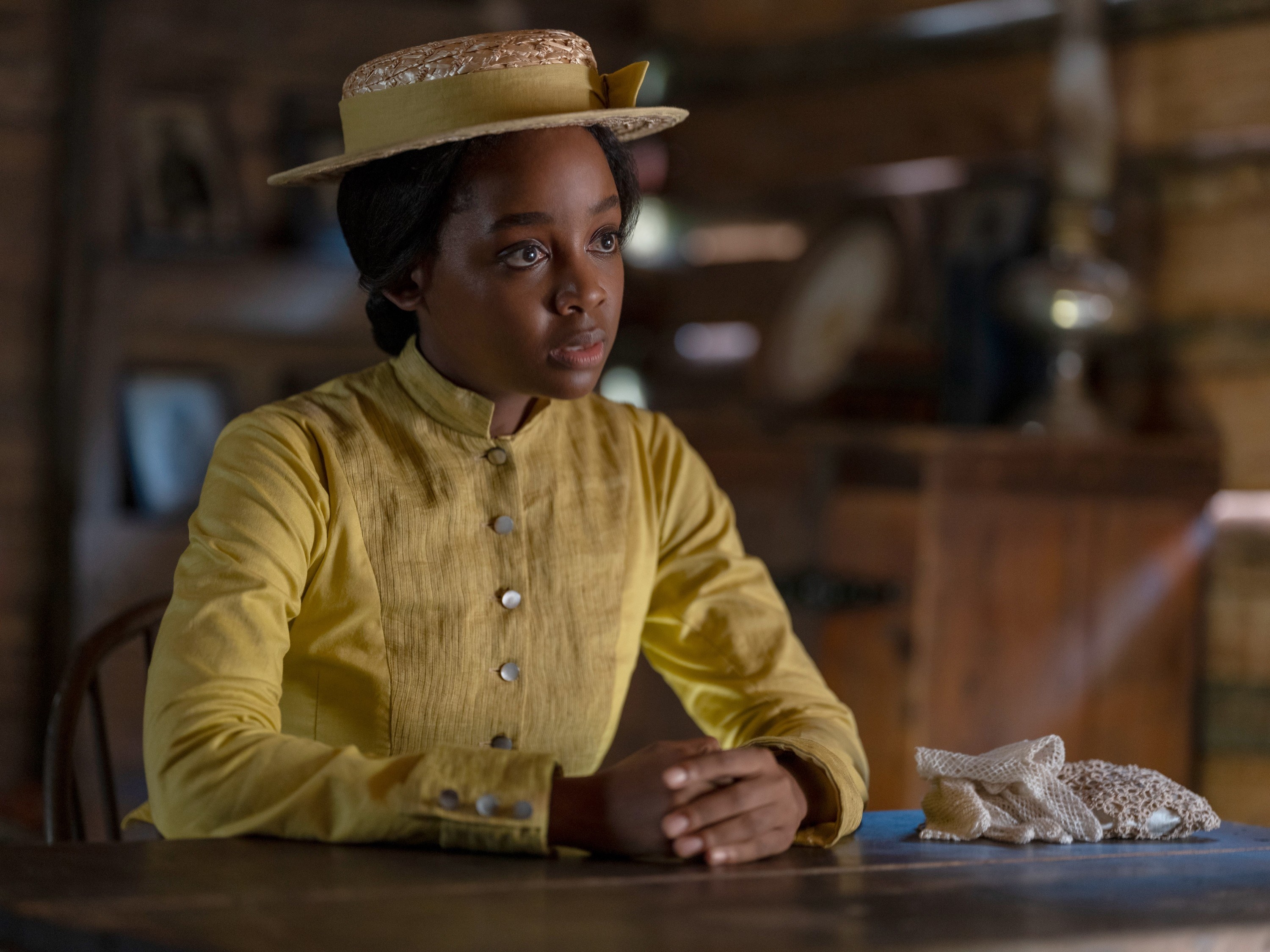 Thuso Mbedu sits at a table wearing a yellow hat and dress