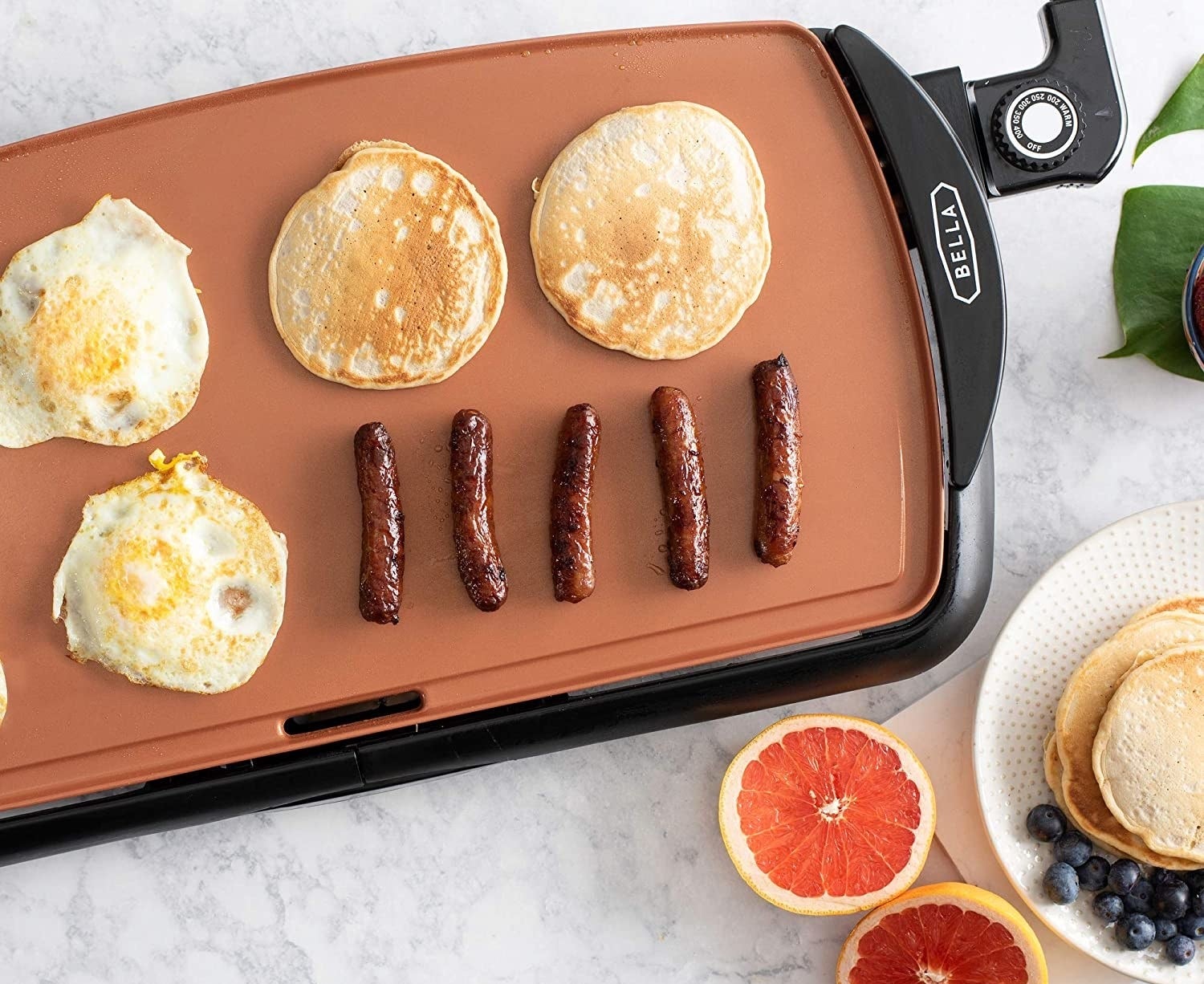 the griddle topped with breakfast food, like pancakes, sausages, and eggs