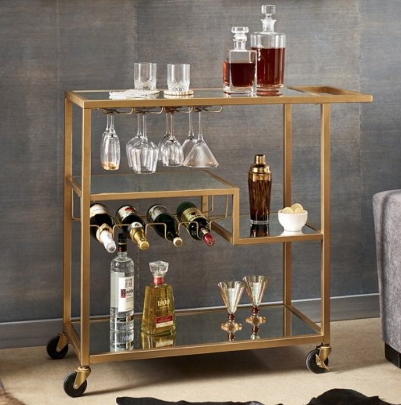 A mirrored/gold bar cart on wheels with 4 shelves, 4 bottle rack, and 4 glass rack