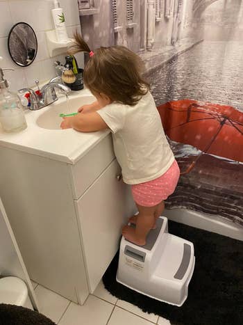 Reviewer's child standing on the stool and brushing their teeth in the sink