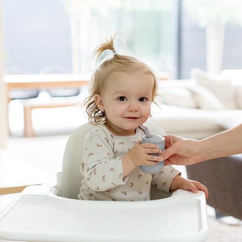 Baby sitting in a high chair and holding the gray silicone cup with straw