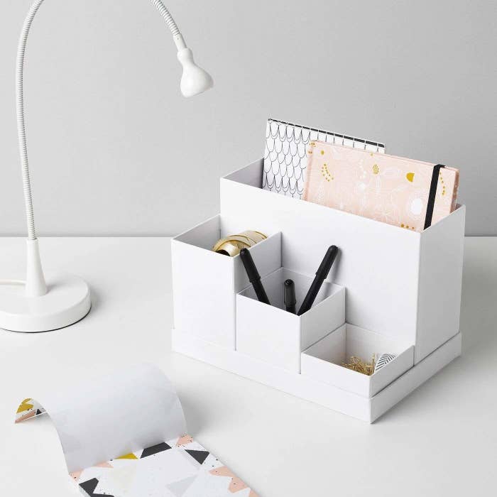 A desk shelf with notebooks and stationery inside, placed on a table next to a lamp