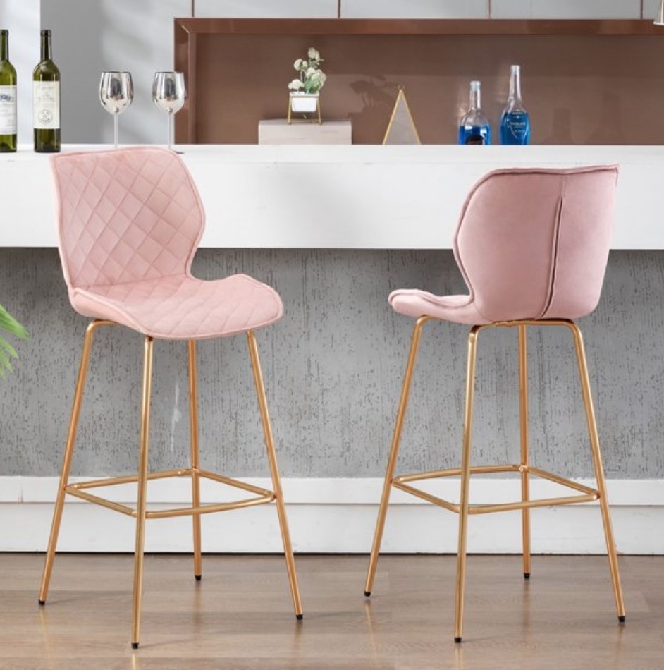 A set of 2 pink tufted bar stools with gold legs at a kitchen counter