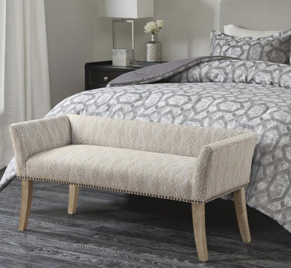 A cream accent bench with nailhead trim at the foot of a bed
