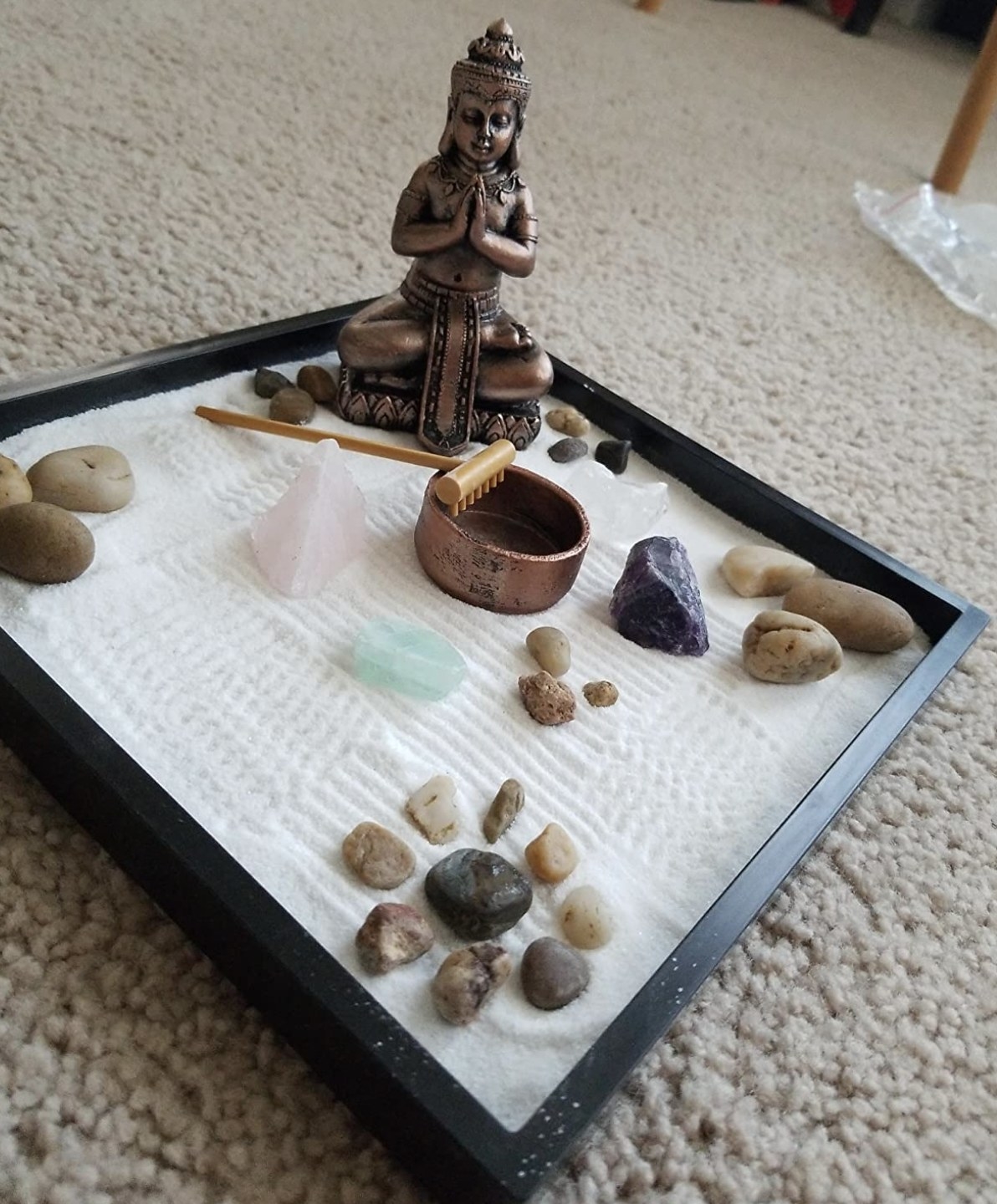 a zen garden with stones, a rake, sand, and a Buddha statue