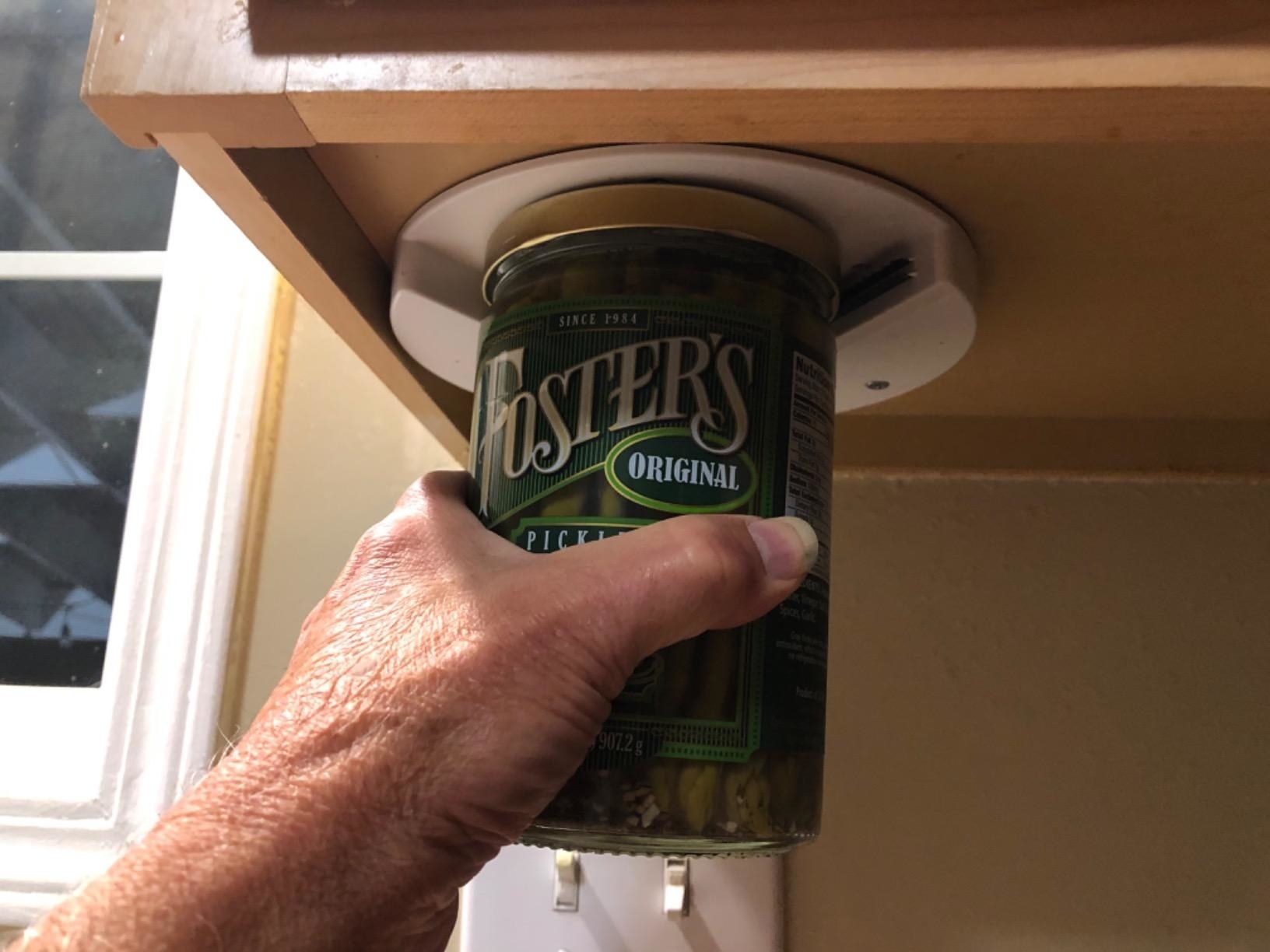 a reviewer&#x27;s hand places a jar into the under-the-counter jar opener