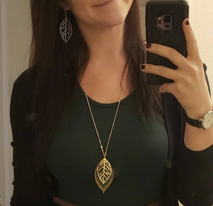 Model wearing a pair of gold dangling leaf earrings and matching gold pendant leaf necklace