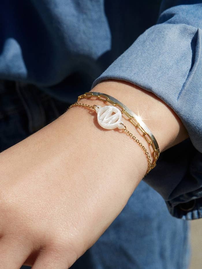 a gold chain bracelet with an acrylic &#x27;m&#x27; on it in white