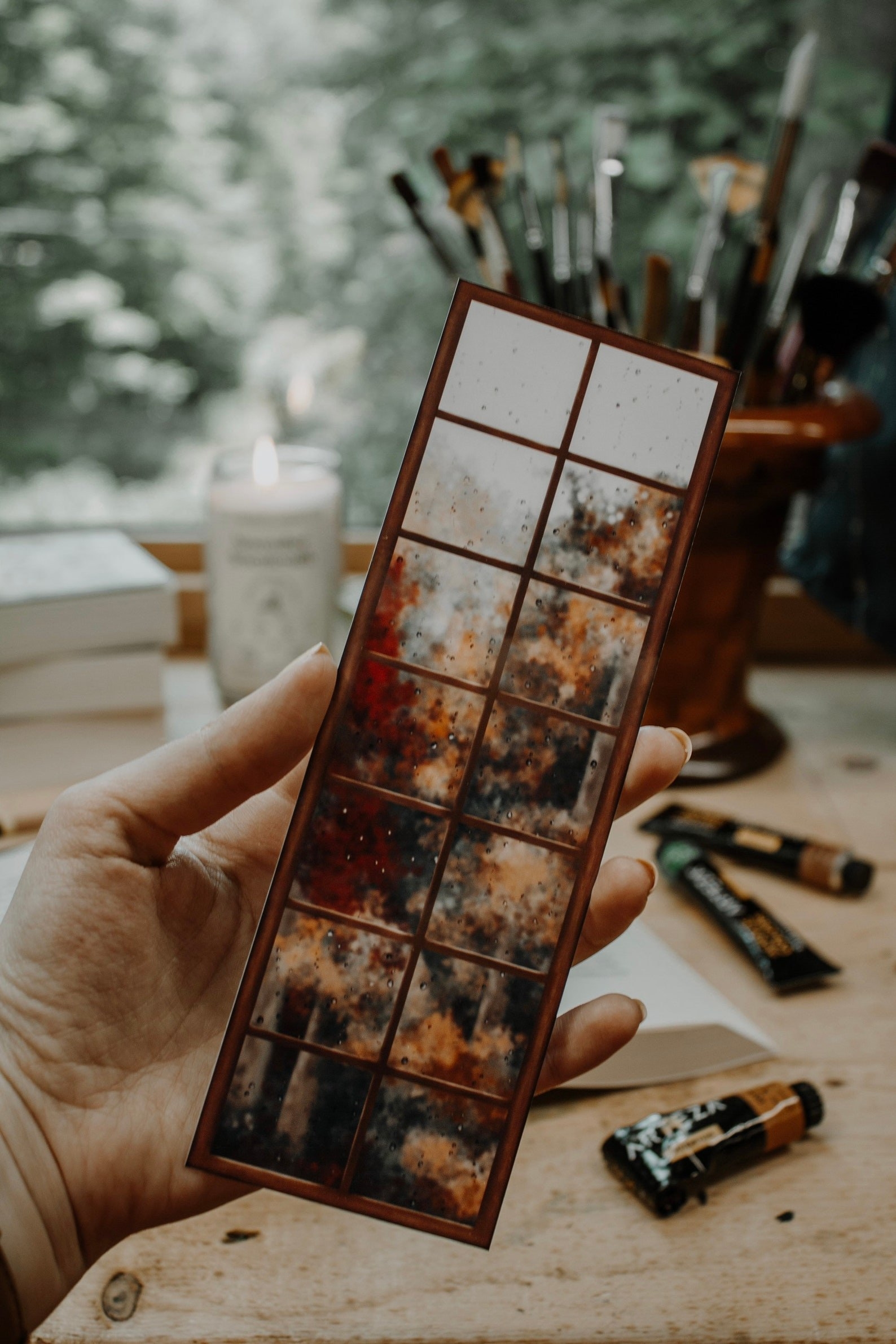 A bookmark with a window pane design that shows a rainy autumn day