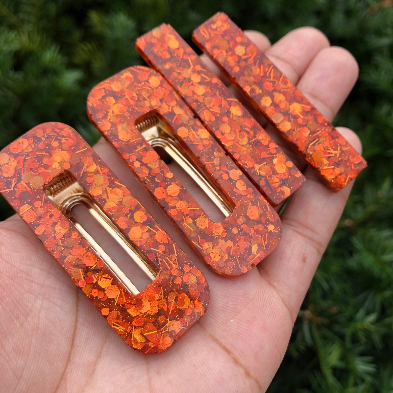 Model holding four hair clips with different shapes and a burnt orange, gold, and brown leaf pattern on them