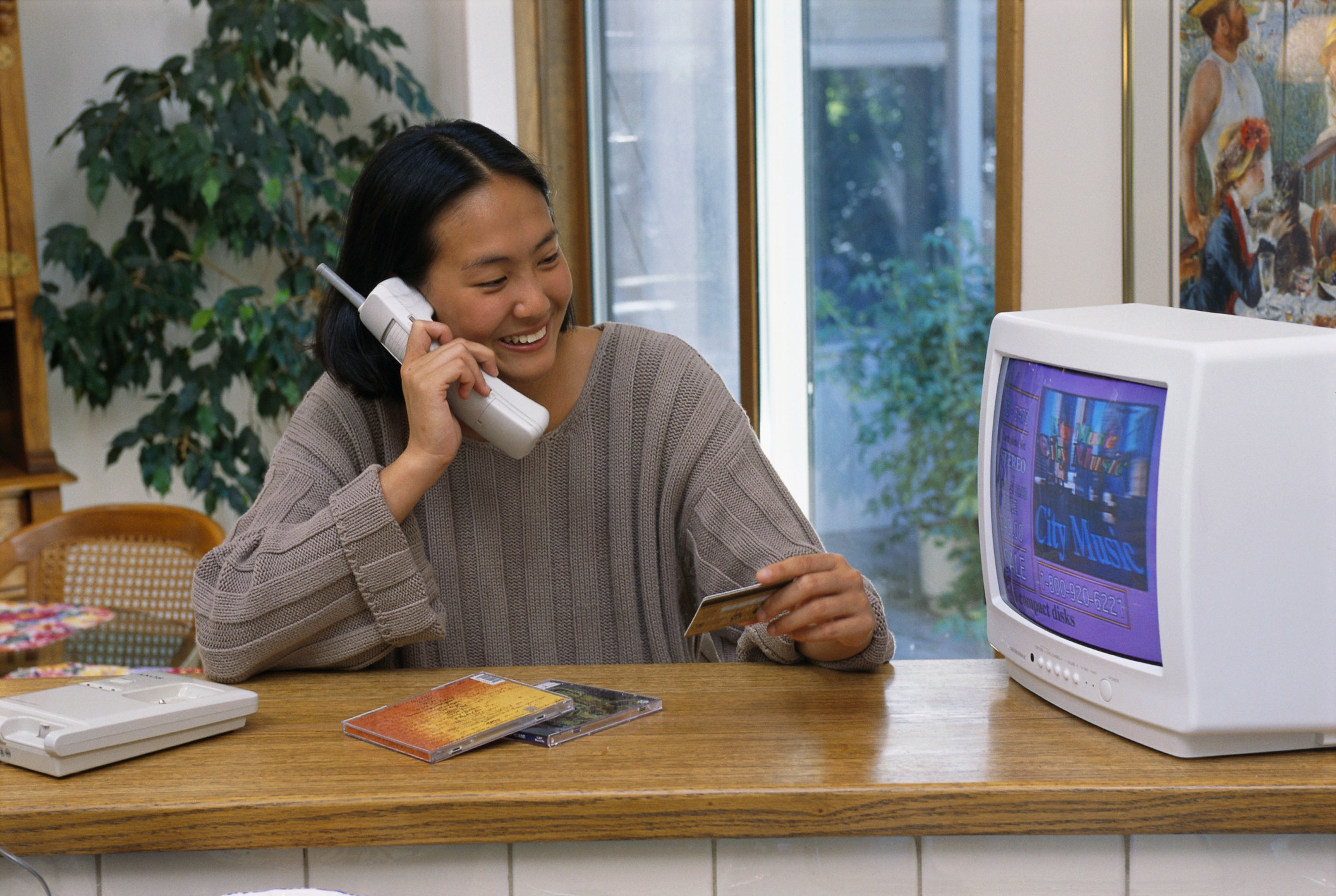 Woman holding a credit card while on the phone and watching TV