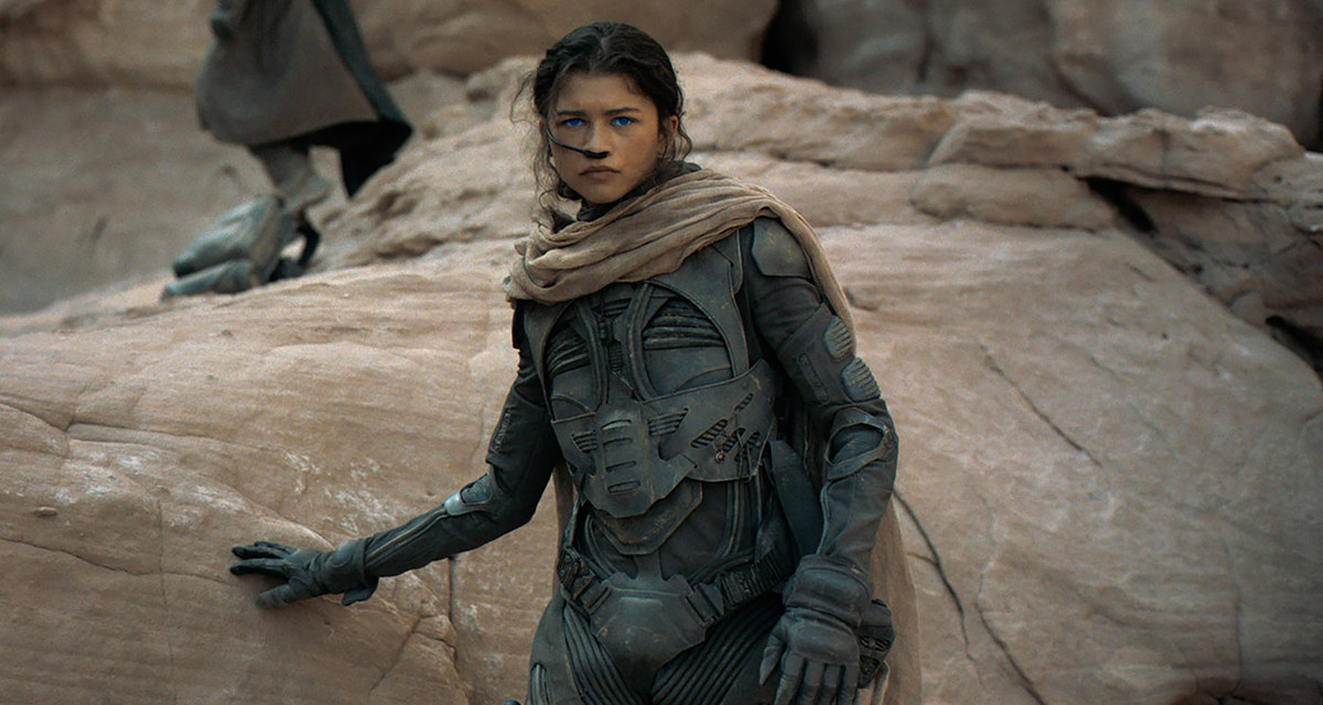 Zendaya in gear as she leans against a rock formation in a scene from Dune