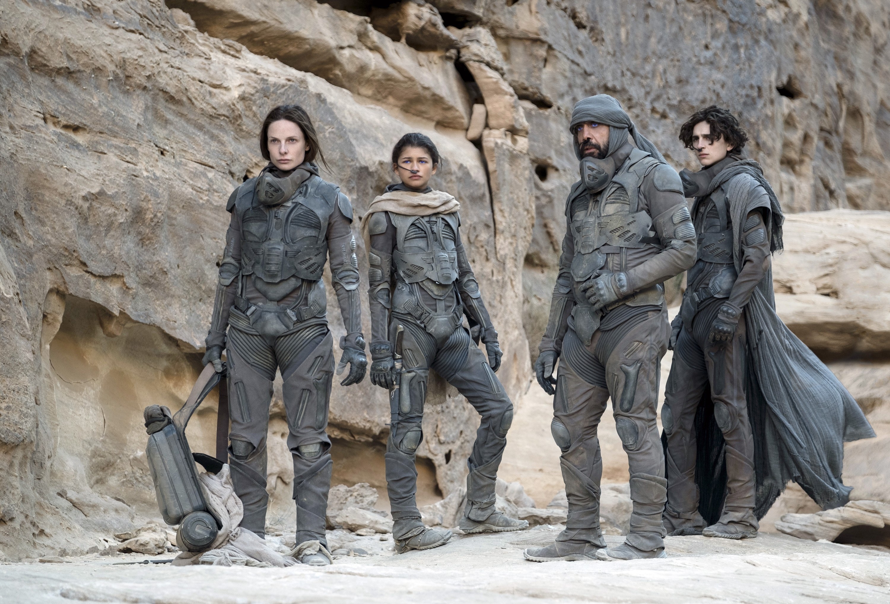Jessica, Chani, Stilgar, and Paul, in survival suits, standing in a large rock formation looking out at something