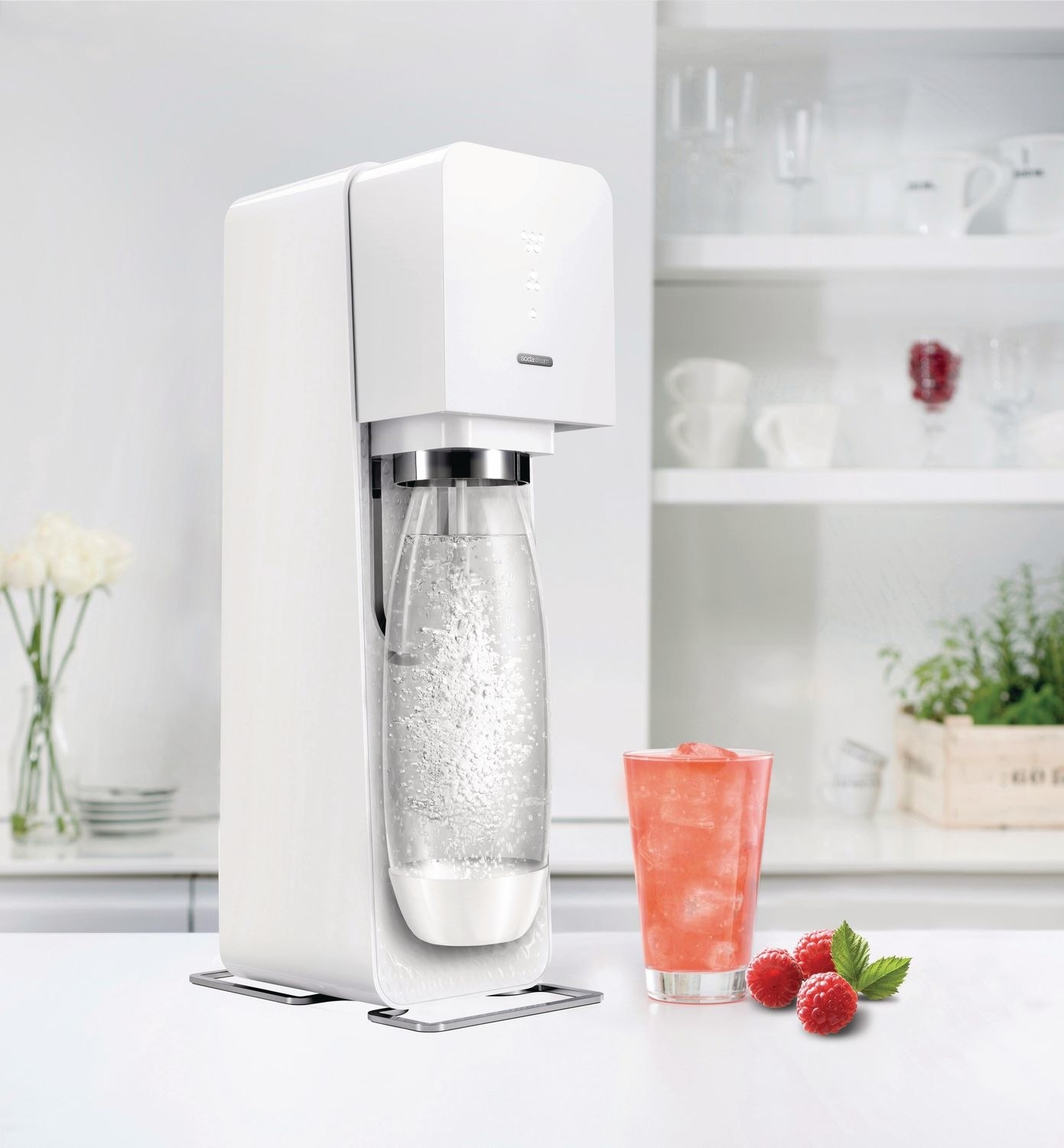 the sodastream on a table with a glass of raspberry drink next to it