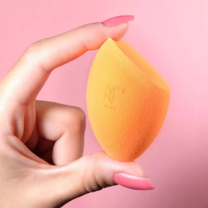 a hand with pink nails holding one of the orange sponges against a pink background