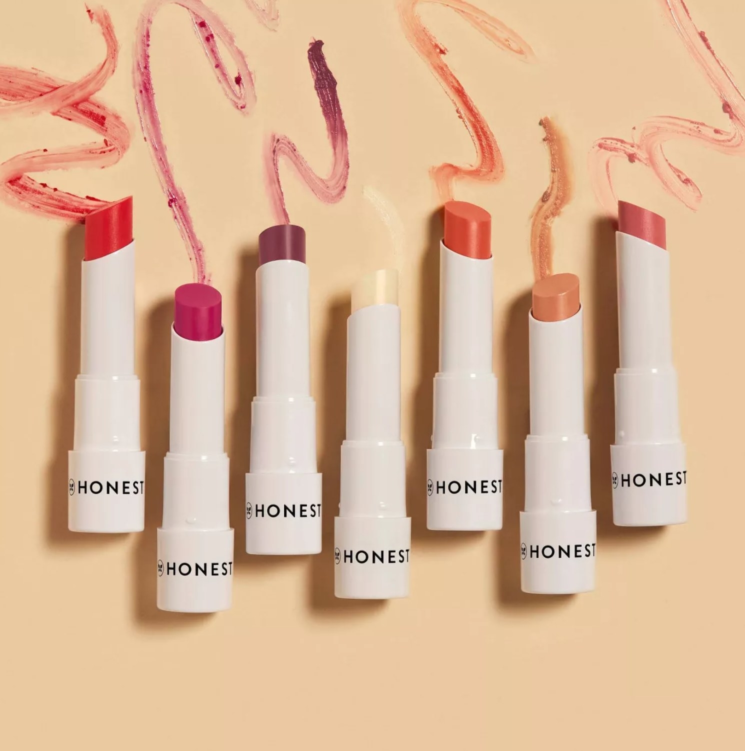 seven of the lip shades set against a tan background with streaks above them to show off the colors