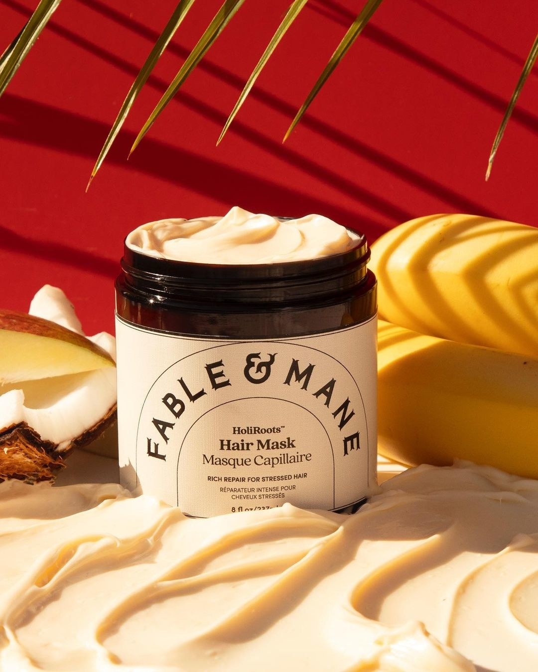 The tub of hair cream surrounded by bananas and coconut