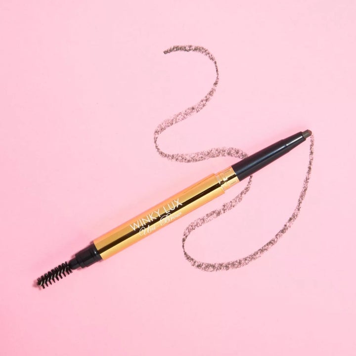 the brow pencil with one brush end and another pencil end set against a pink background with a squiggly line from the pencil side