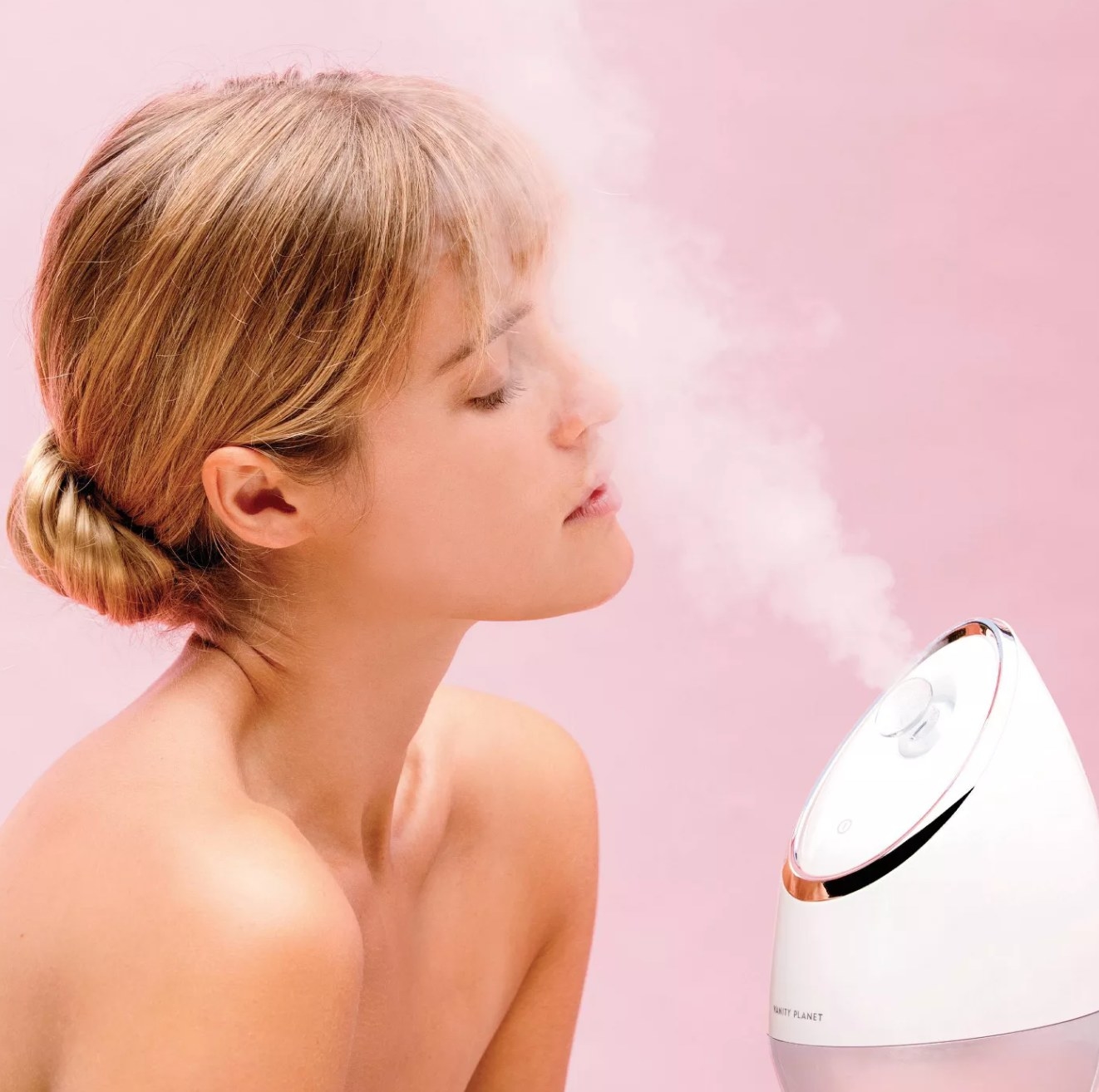 a model using the facial steamer against a pink background