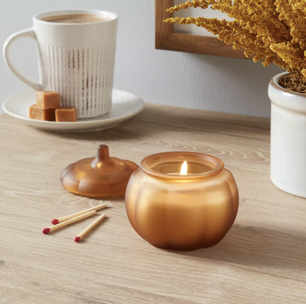 An amber colored pumpkin shaped mini candle lit on a table