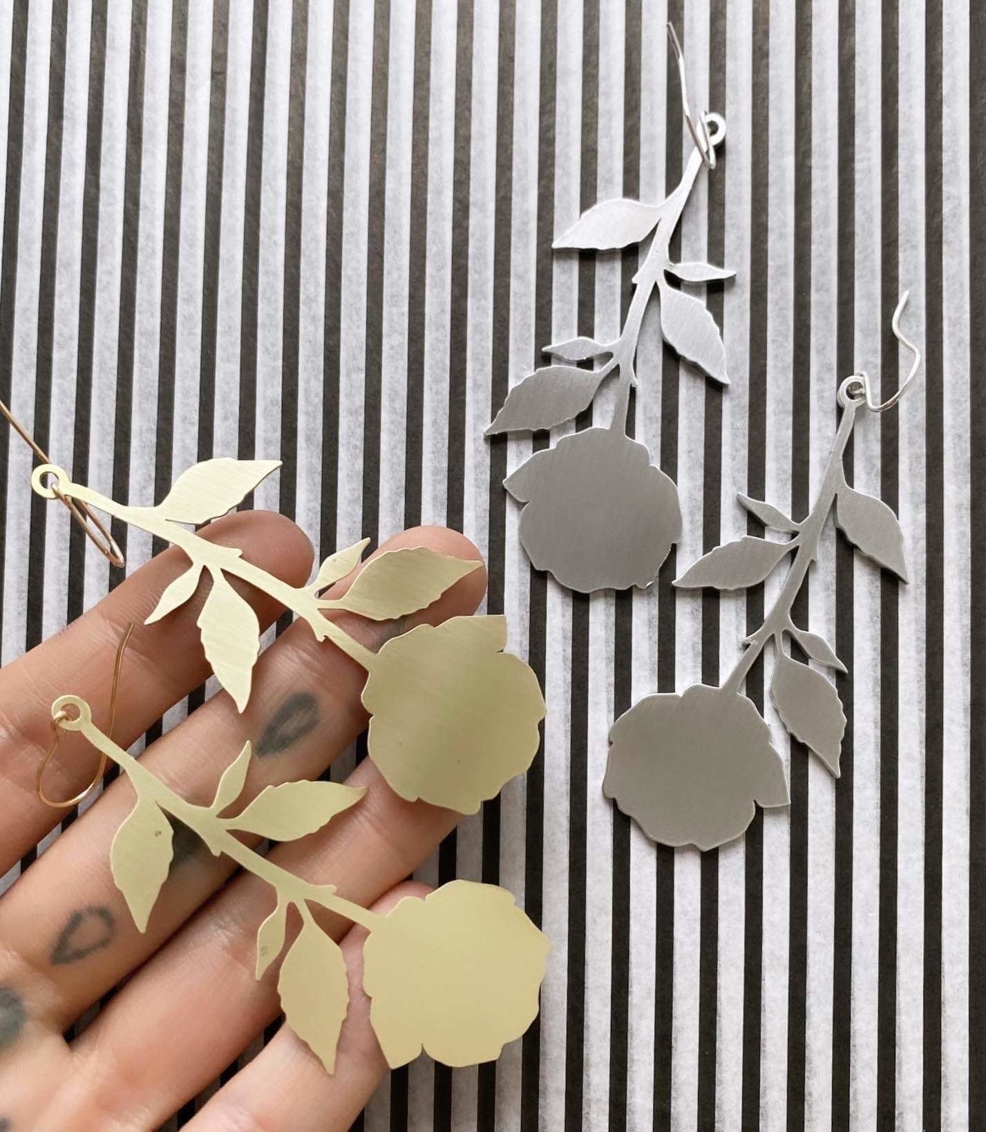 Model holding gold rose-shaped earrings next to silver rose-shaped earrings