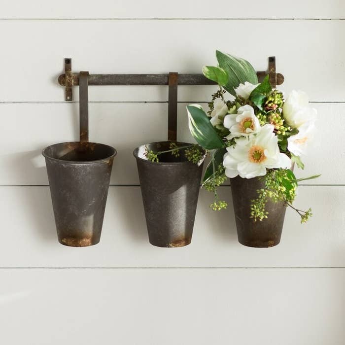Product image of three metal rustic hanging pots with the far right one filled with a mix of white flowers