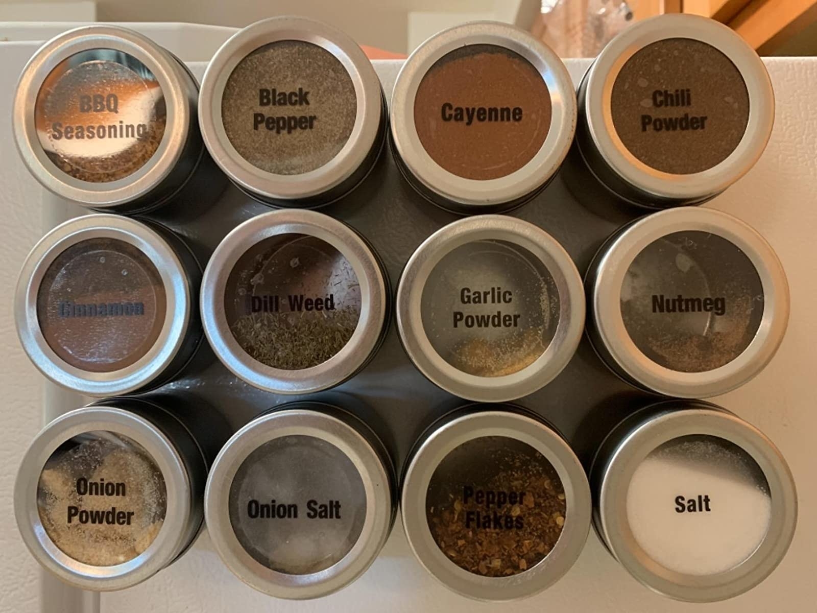 Reviewer photo of 12 silver and clear magnetic spice containers attached to the side of a fridge and labeled &quot;BBQ seasoning&quot;, &quot;black pepper&quot;, &quot;cayenne&quot;, etc