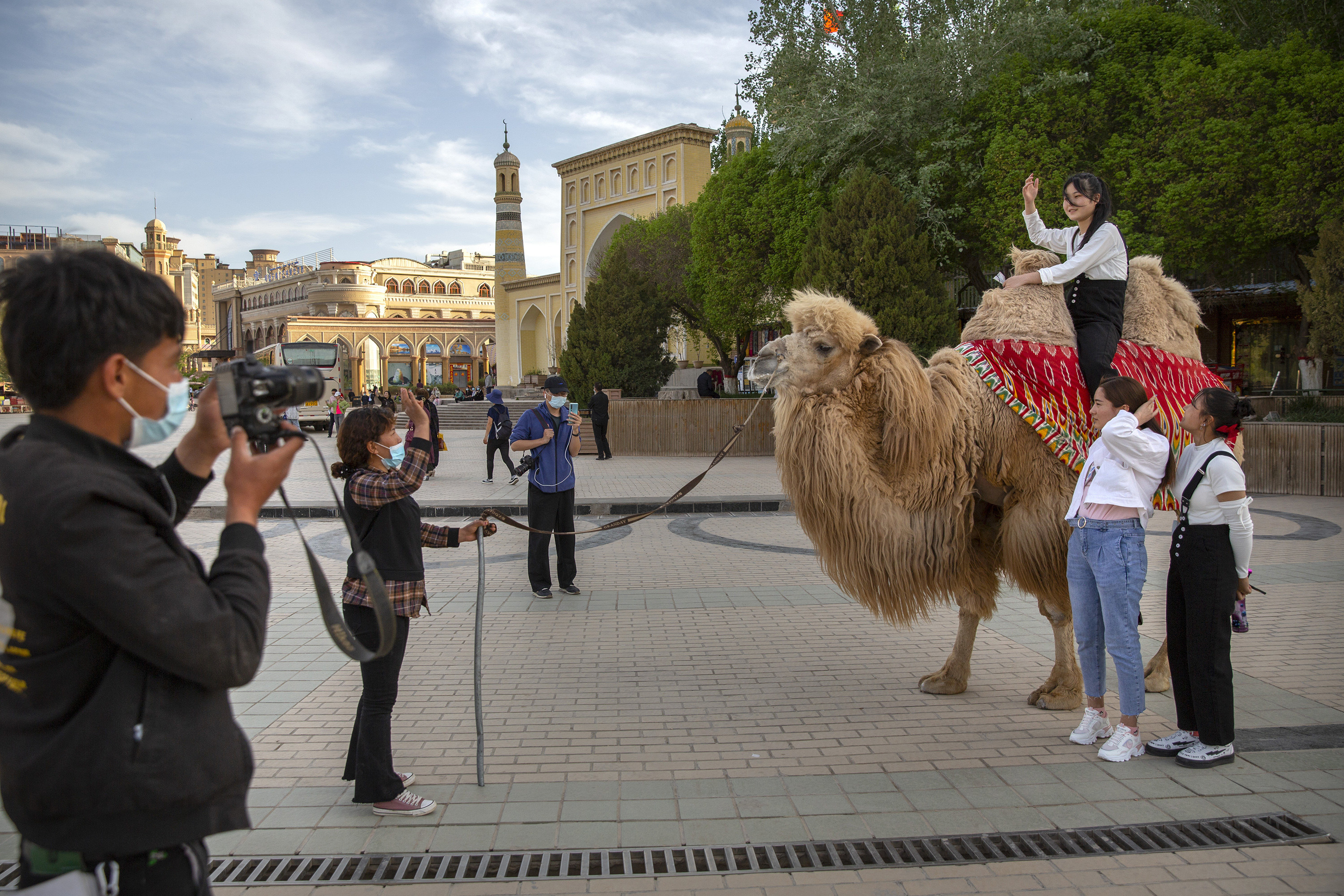 Photographers take a picture of three teenage girls, one of them sits on a camel