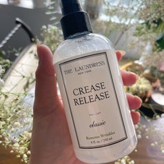 a person holding up a bottle of the wrinkle-releasing mist against a backdrop of baby's breath flowers