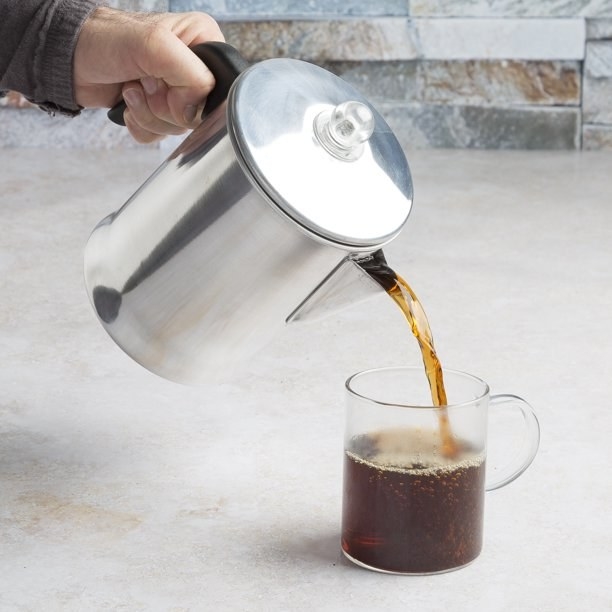 Model pouring coffee from silver stovetop percolator into a clear mug