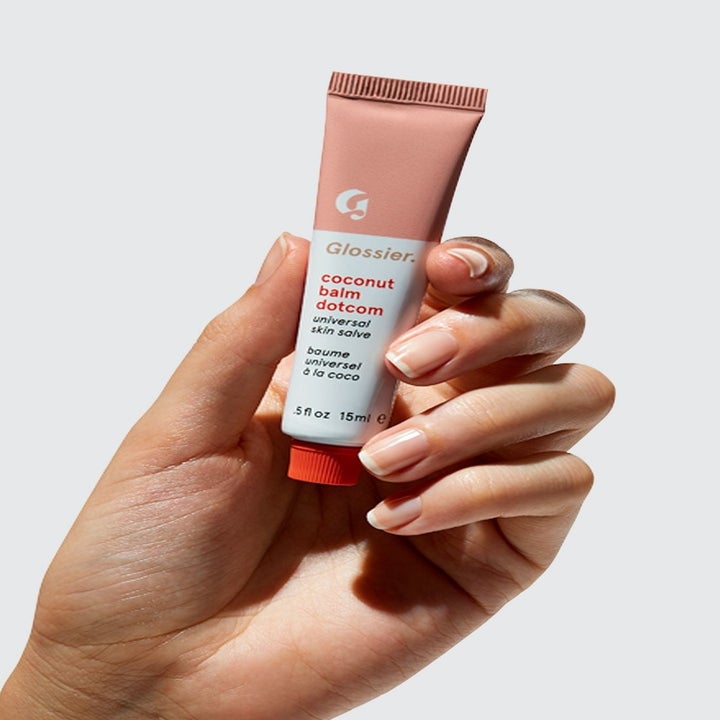 A hand holding up the Glossier Balm Dotcom in Coconut
